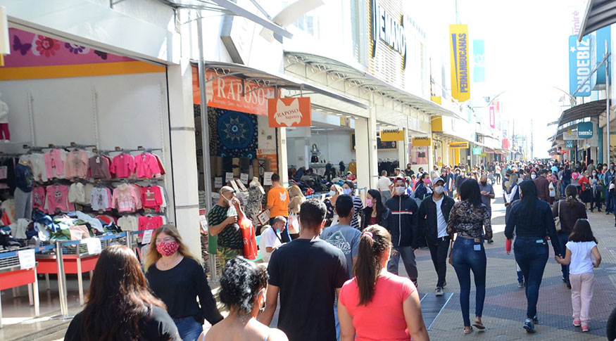 #PraCegoVer Pedestres caminham nas ruas, usando máscaras de proteção, para aproveitar a reabertura do comércio