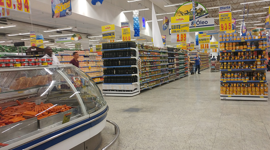 #PraCegoVer A foto mostra à esquerda um balcão de supermercado com salcichas, o resto da imagem mostra corredores do supermercado