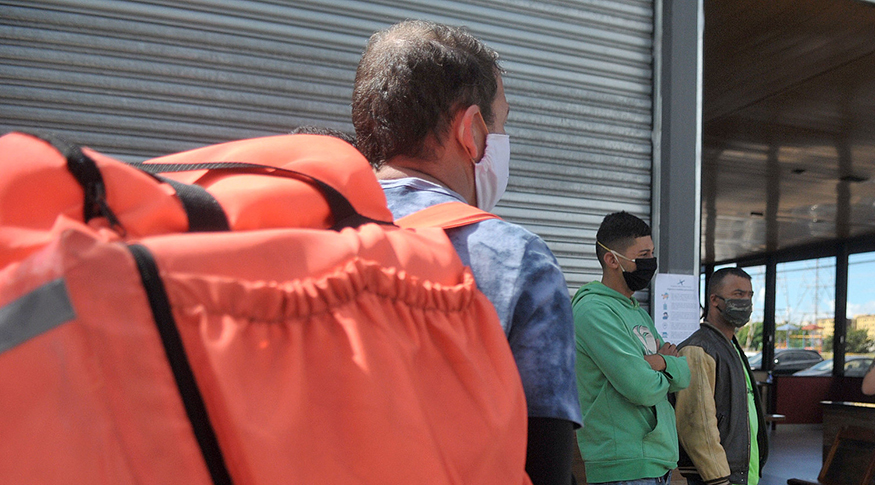 #PraCegoVer A foto mostra alguns entregadores reunidos com suas bolsas de cor laranja, nas costas.