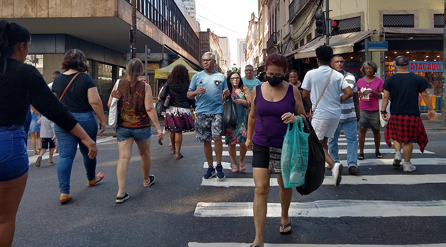 #PraCegoVer A foto mostra muitas pessoas atravessando a rua na faixa de pedestre.