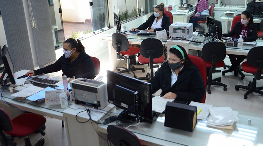 #PraCegoVer A foto mostra pessoas trabalhando em escritório, todas usando máscaras para se protegerem contra o Covid-19