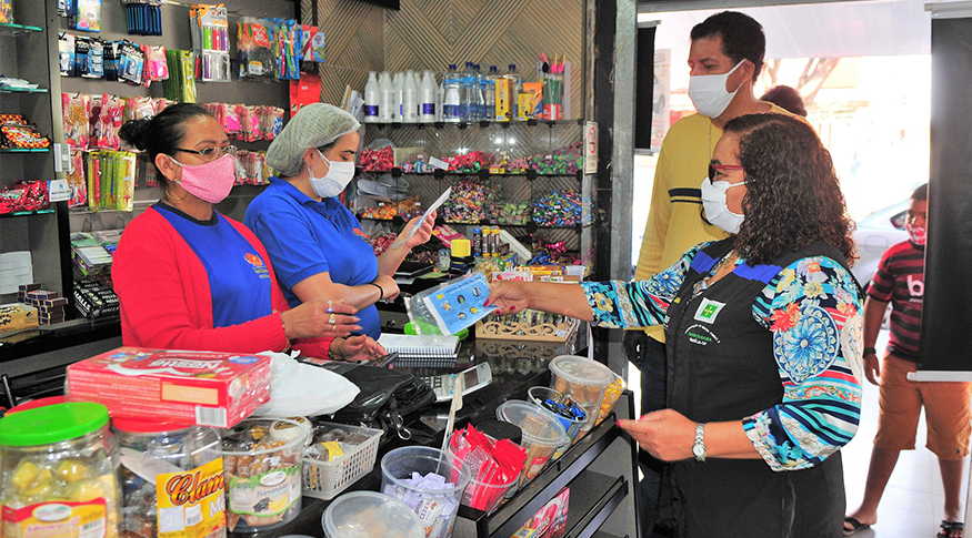#PraCegoVer Após a retomada das vendas no comércio, a foto mostra uma pequena loja de balas, com alguns clientes de máscara sendo atendidos no balcão
