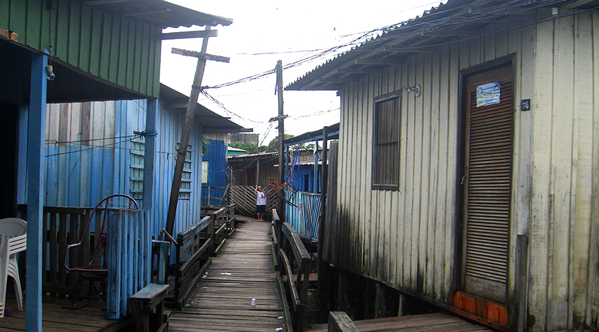 #PraCegoVer A foto mostra casas de madeira simples em Manaus