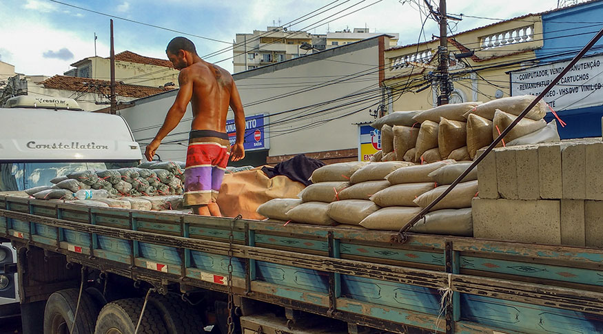 #PraCegoVer operário sobre o caminhão com materiais de construção