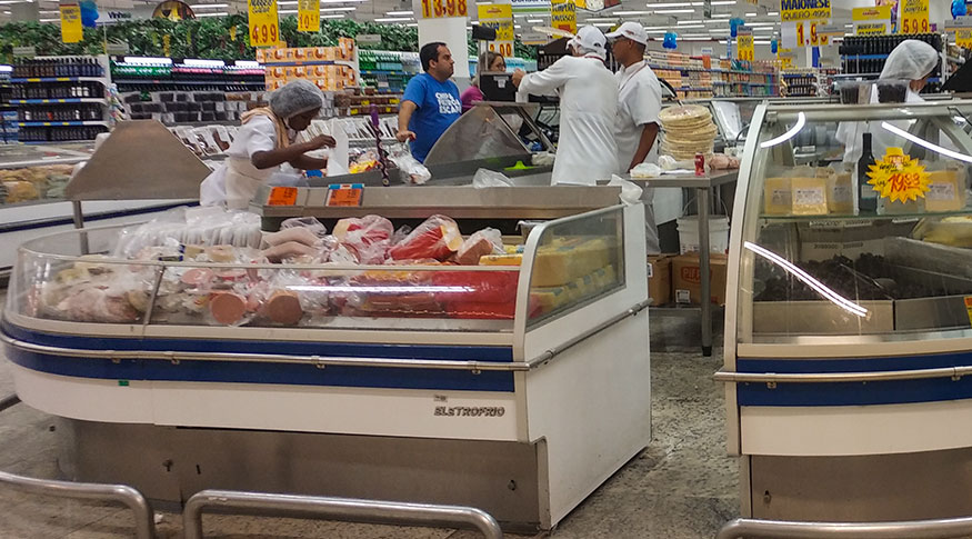 #PraCegoVer A foto mostra o interior de um supermercado, com suas prateleiras e pessoas circulando com carrinhos de compras
