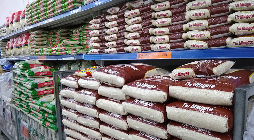 #PraCegoVer A foto mostra as prateleiras de um supermercado, com vários pacotes de arroz, de diversas marcas.