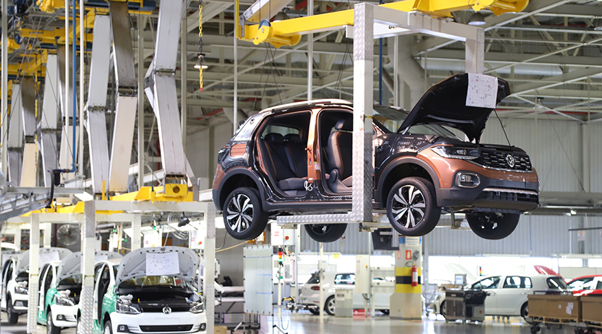 #pracegover a foto mostra o interior de uma fábrica de veículos e um carro de cor marrom, pendurado, em fabricação.