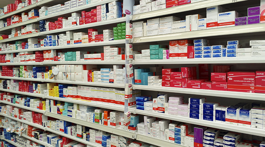 #PraCegoVer A foto mostra prateleiras de farmácia com caixas de remédios de diversas cores.