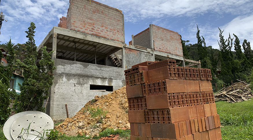 #PraCegoVer A foto mostra em primeiro plano vários tijolos empilhados. Ao fundo, mostra parte de uma obra de edificação.
