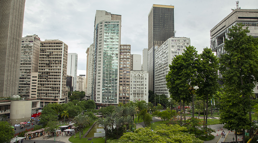 #PraCegoVer A foto mostra uma vista aérea de prédios e de uma praça numa grande cidade.