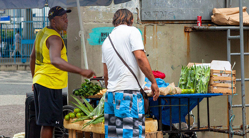 #PraCegoVer foto de vendedor na sua barraca de verduras  atendendo um comprador 