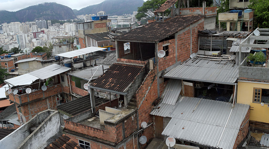 #PraCegoVer Casas de favela no primenri plano e ao fundo prédios mais ao longe um morro e céu nublado
