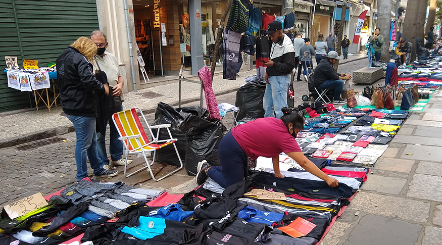 #PraCegover A foto mostra uma sequencia de mercadorias expostas na rua, sendo vendidas por ambulante.